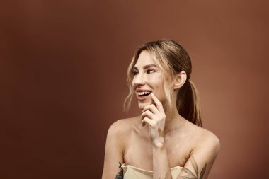 Vitiligo 'su ve dövmesi olan genç bir kadın parlak bir şekilde gülümsüyor, çıplak omuzları bej bir arka plana karşı açıkta..