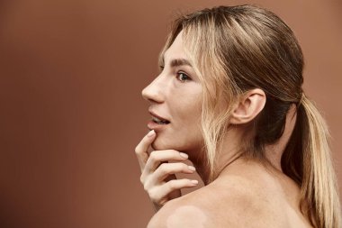 Vitiligo 'su olan genç bir kadın bej arka planda poz veriyor. Çıplak bir omuz giyiyor ve saçları at kuyruğu şeklinde geri çekiliyor..