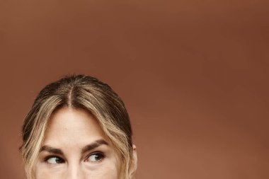 Kendine güvenen genç bir kadın, sıcak bir bej arka planda kamera karşısına geçer..
