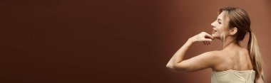 Vitiligo 'su olan genç bir kadın omuzları açık duruyor, bej bir arka plana karşı güvenle poz veriyor..
