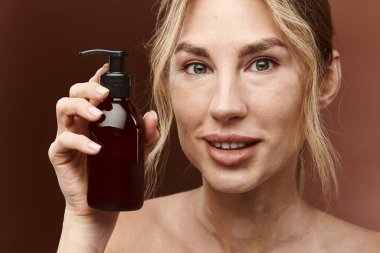 Vitiligo 'su olan genç bir kadın bej arka planda bir şişe cilt ürünü tutuyor..