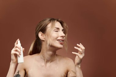 Vitiligo 'su olan genç bir kadın elinde bir cilt bakım ürünü tutuyor ve bej bir arka plana gülümsüyor..