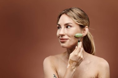 Vitiligo 'su olan genç bir kadın cilt bakımının bir parçası olarak yüzüne yeşim bir silindir takıyor. Arka plan yumuşak bir bej..