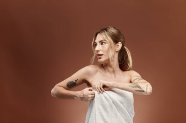 Vitiligo 'su olan genç bir kadın havluyla duruyor, omzunun üstünden bakarken havluyu ayarlıyor..