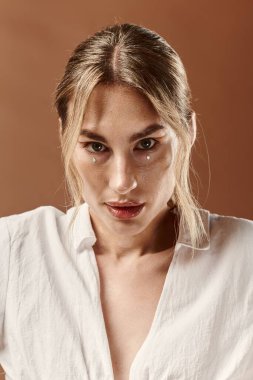 Beyaz tişörtlü, kendine güvenen genç bir kadın bej arka planda kendini beğenmişlik ve doğal güzellikle parlıyor..