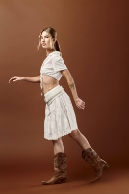 Vitiligo 'su olan genç bir kadın beyaz bir yaz elbisesi içinde kahverengi bir arka planda poz veriyor..