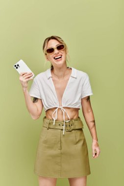 A young woman with vitiligo poses in a white summer outfit against a green background. She smiles and holds a phone, radiating confidence. clipart