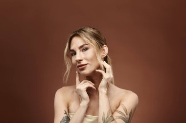 A young woman with vitiligo and a tattoo poses with her shoulders bare against a beige background. clipart