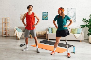 Woman with prosthetic leg and boyfriend prepare to workout on yoga mats at home. clipart