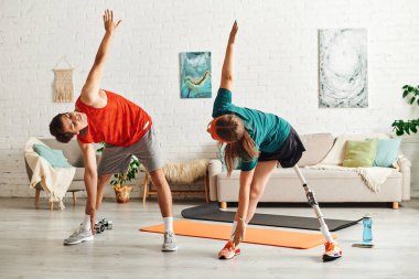 A woman with a prosthetic leg stretches with her boyfriend in their living room. clipart