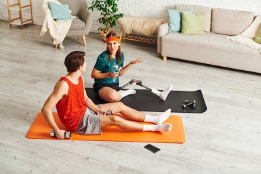 Ev ortamında yoga minderleri üzerinde dambıllarla birkaç egzersiz. Kadının protez bacağı var..