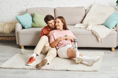 Couple in love on a fluffy rug, woman with prosthetic leg. clipart