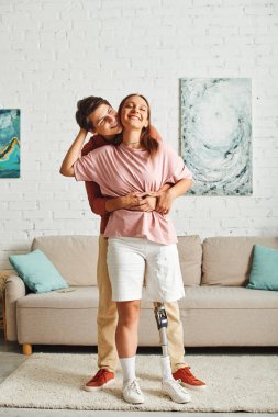 A woman with a prosthetic leg embraces her boyfriend in a living room. clipart