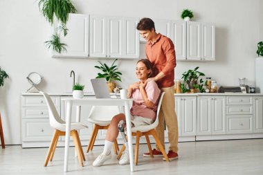 A woman with a prosthetic leg smiles and laughs with her boyfriend in their kitchen. clipart