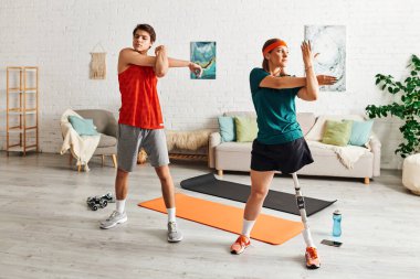 Protez bacaklı bir kadın ve erkek arkadaşı oturma odasındaki yoga minderlerinde esniyorlar..