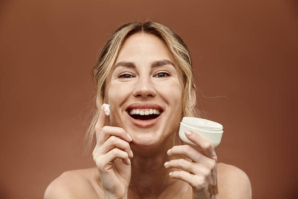 Молодая женщина с витилиго ярко улыбается, когда она наносит увлажняющий крем на лицо, демонстрируя свою красивую и уникальную кожу.