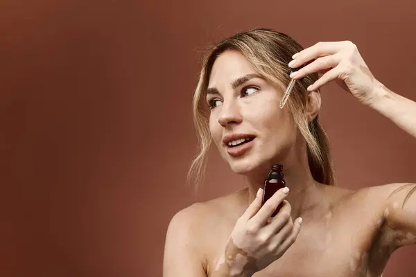 stock image A young woman with vitiligo is applying a skin care product to her face. She is smiling and looks happy.