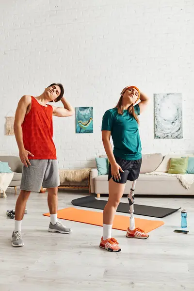 Stock image A woman with a prosthetic leg stretches alongside her boyfriend in their home gym.