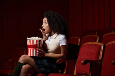 Gündelik giyinmiş siyah bir kadın sinemada filmi izlerken şok olmuş gibi görünür..