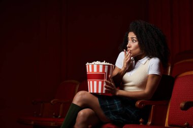 Genç bir Afrikalı Amerikalı kadın sinemada oturuyor, filme dalmış, elinde patlamış mısırla..