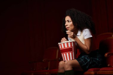Genç bir kadın sinema koltuğunda oturuyor, bir filme dalmış, yüzünde bir beklenti ifadesi var..
