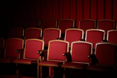 Rows of empty red velvet seats in a darkened movie theater, anticipation hangs in the air. clipart