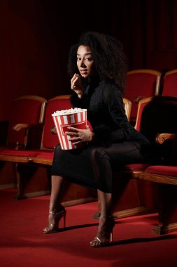 Filmdeki son moda Afrikalı Amerikalı kadın, patlamış mısırla şık görünüyor, filme dalmış..