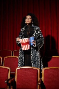 Leopar desenli Afro-Amerikan kadın elinde patlamış mısır ve içecekle sinemada filme tepki veriyor..