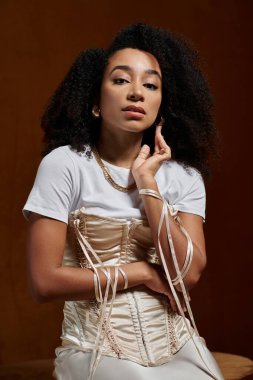 Moda kıyafetli şık bir Afrikalı Amerikalı kadın, kahverengi bir fona karşı poz veriyor..