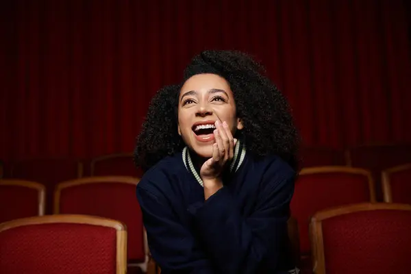 stock image A young woman in stylish casual clothes laughs in delight while watching a movie in a cinema.