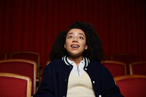 stock image A young woman in a movie theater, with a wide-eyed expression of surprise as she watches a film.