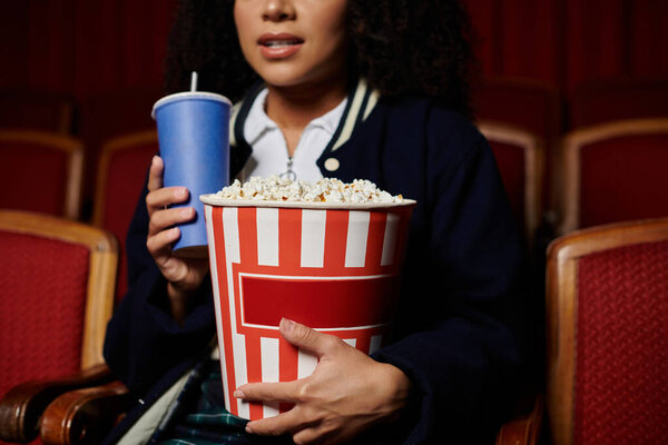 A young woman enjoys popcorn and a drink while watching a movie.