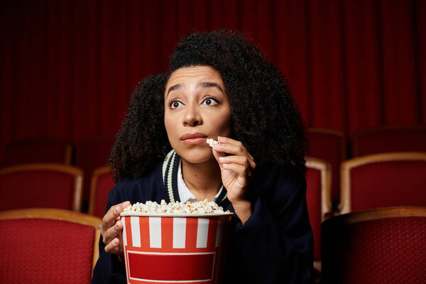 A young woman in a cinema, eyes glued to the screen, reacts to a thrilling moment in the movie.