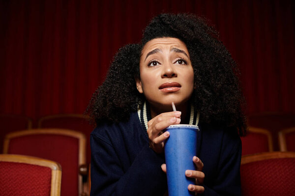 A young woman with curly hair watches a movie in a theater, captivated by the action on screen.