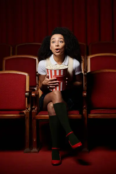 stock image A young woman sits in a cinema seat, eyes wide with surprise as she watches the movie.