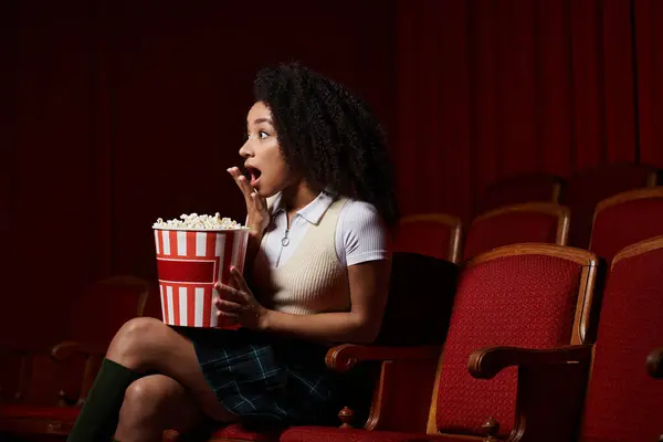 stock image A Black woman in casual attire looks shocked in a movie theater as she watches the film.