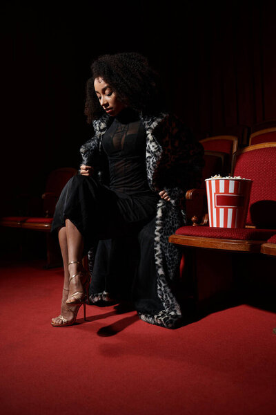 Стильная женщина в леопардовом пальто сидит в затемненном кинотеатре, погруженная в фильм, играющий на экране.