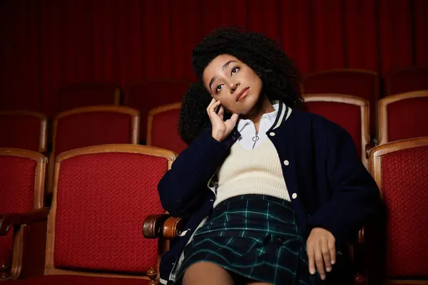 stock image A young woman in stylish attire sits engrossed in a movie, her expression revealing the film captivating power.