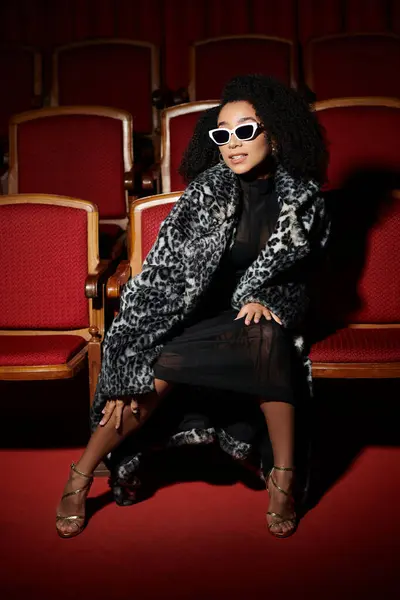 stock image A stylish African American woman wearing a leopard print coat and sunglasses watches a movie in a cinema.