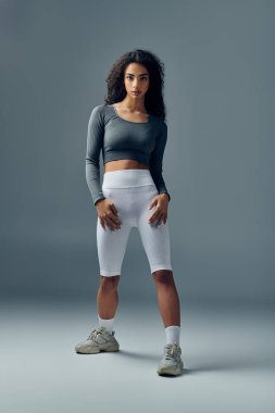 Spor kıyafetleri içinde genç bir Afrikalı Amerikalı kadın stüdyo ortamında güvenle duruyor..