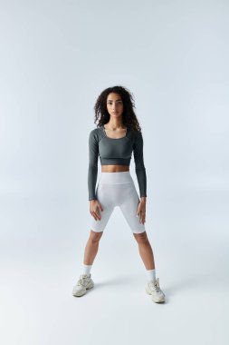 Spor kıyafetleri içindeki genç bir kadın, ayakları ayrık bir şekilde fitness pozisyonunda durur..