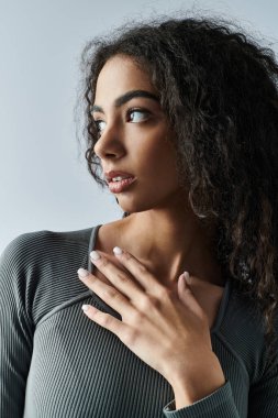 Kıvırcık saçlı ve kararlı bakışlı genç bir kadın bir stüdyoda duruyor, eli göğsünde dinleniyor..