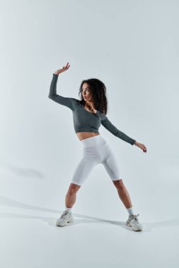 Spor kıyafetleri içinde genç bir Afrikalı Amerikalı kadın beyaz bir zemine karşı poz veriyor, atletizm ve formda olduğunu gösteriyor..