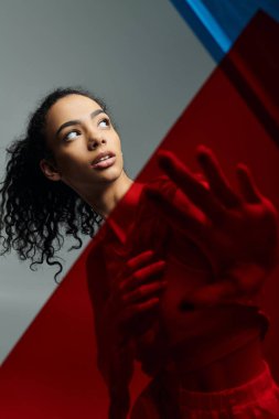 A young African American woman with curly hair poses in a studio, with red light illuminating her from behind. clipart