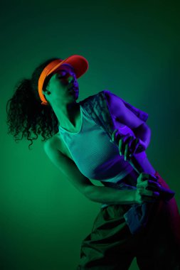 A young woman poses in a studio with neon lights, wearing a visor and a white top. clipart