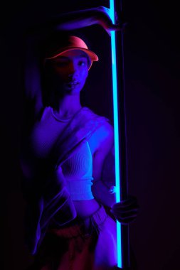 Genç bir kadın neon ışıklı bir stüdyoda, silueti parlak mavi ışıklarla aydınlatılıyor..