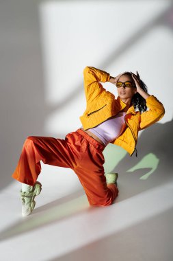 Sarı ceketli ve turuncu pantolonlu şık bir genç kız stüdyoda poz veriyor..