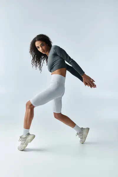 stock image A young woman in athletic wear performs a dynamic stretch against a white backdrop.