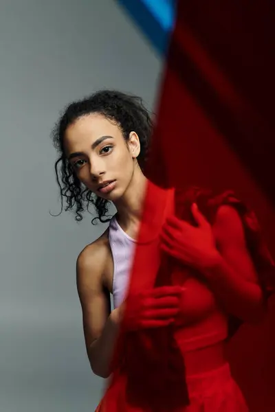 stock image A young Black woman, dressed in workout clothes, stands in a studio with a red light behind her, her dark curls cascading down her back.