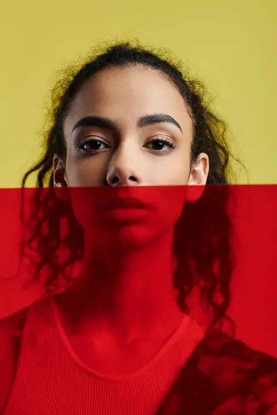 stock image A young woman with dark curly hair poses against a bright yellow background in a studio setting.